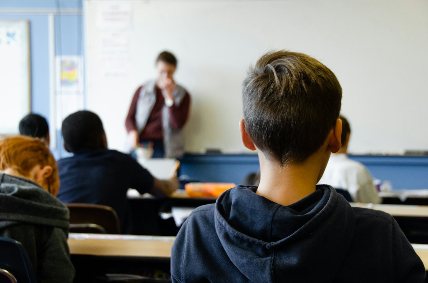 Pupils at their desks, seen from the back of the classroom, listening to their teacher