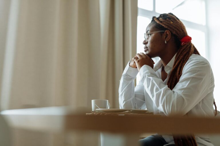 pensive woman in white dress shirt sitting by the table
